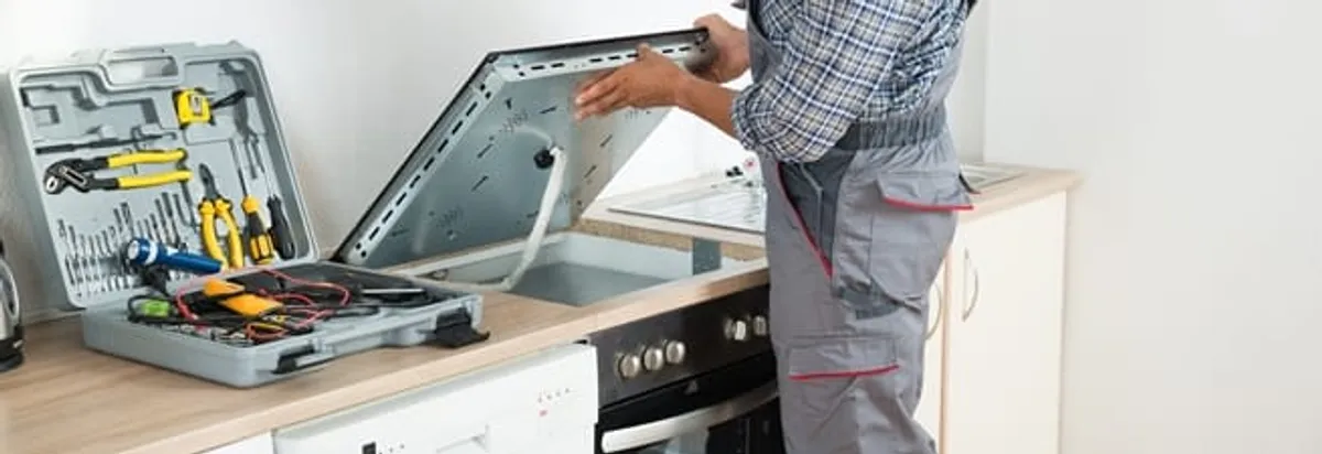 Cooktop repair technician lifting a built-in stovetop for service in Green Bay, WI